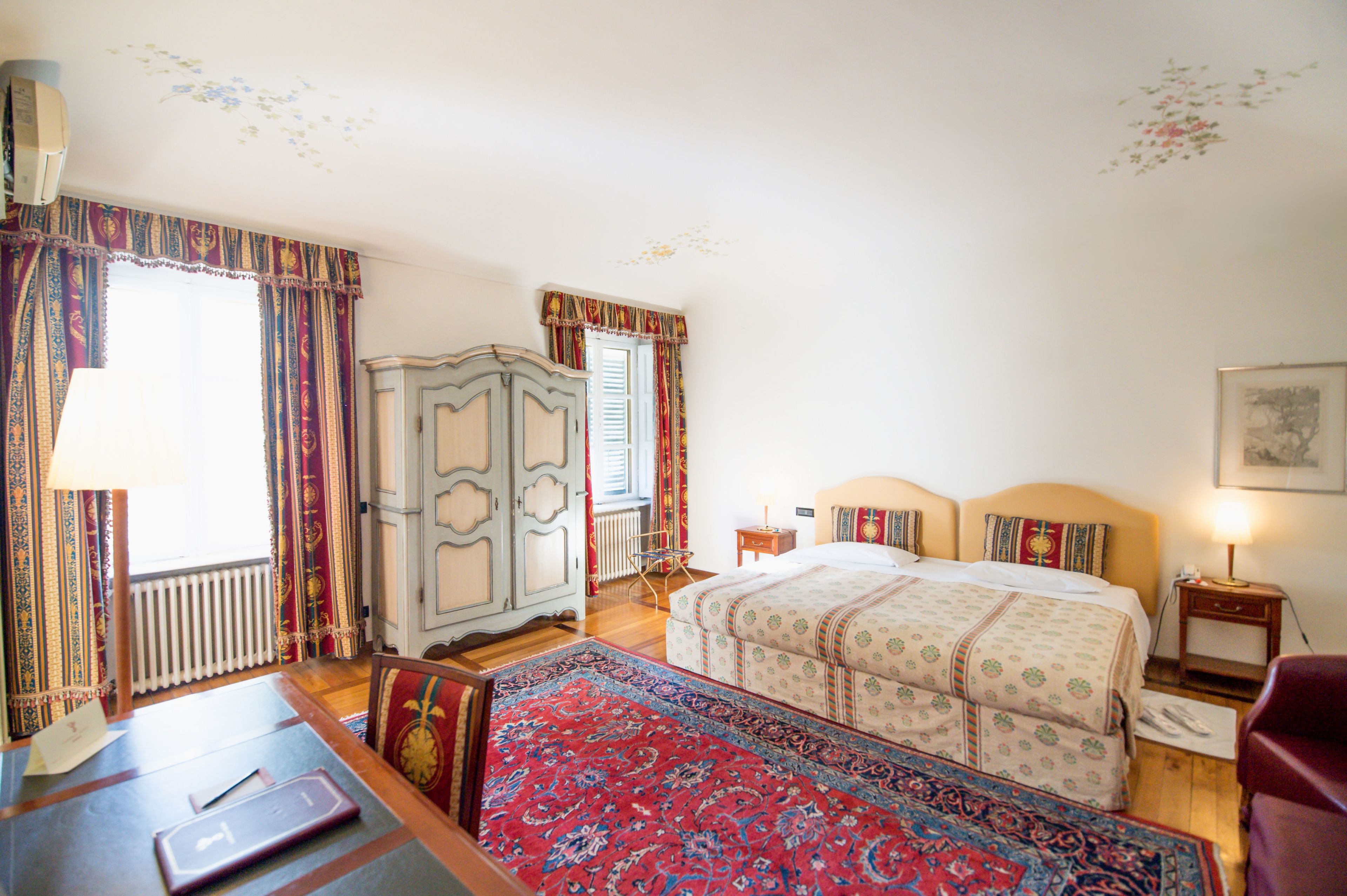 A hotel room with a large bed, a wooden dresser, a desk with a chair, and a red carpet.
