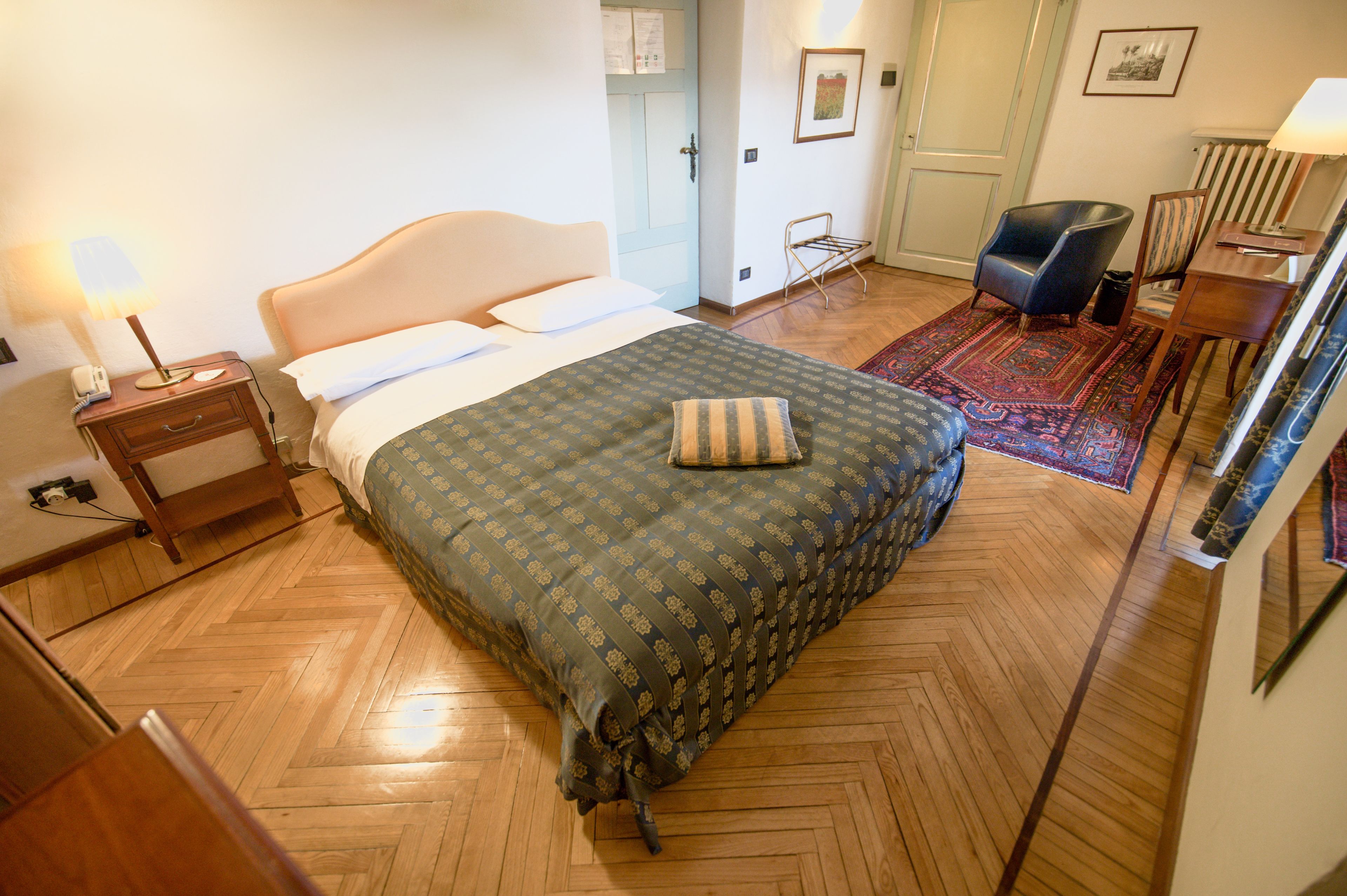 A bedroom with a bed, a nightstand, a chair, a desk, and a radiator.