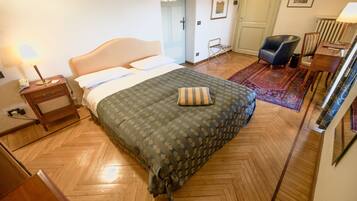 A bedroom with a bed, a nightstand, a chair, a desk, and a radiator.