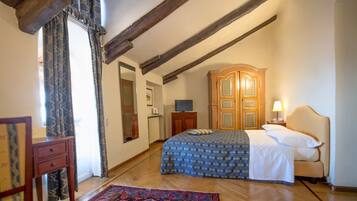 A bedroom with a wooden ceiling, a bed with a patterned bedspread, a wooden wardrobe, a television, and a bedside table with a lamp.