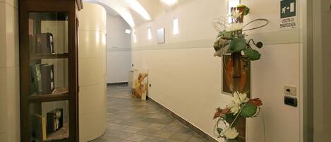 A hallway with a wooden bookshelf, a floral arrangement, and a sign indicating an emergency exit.