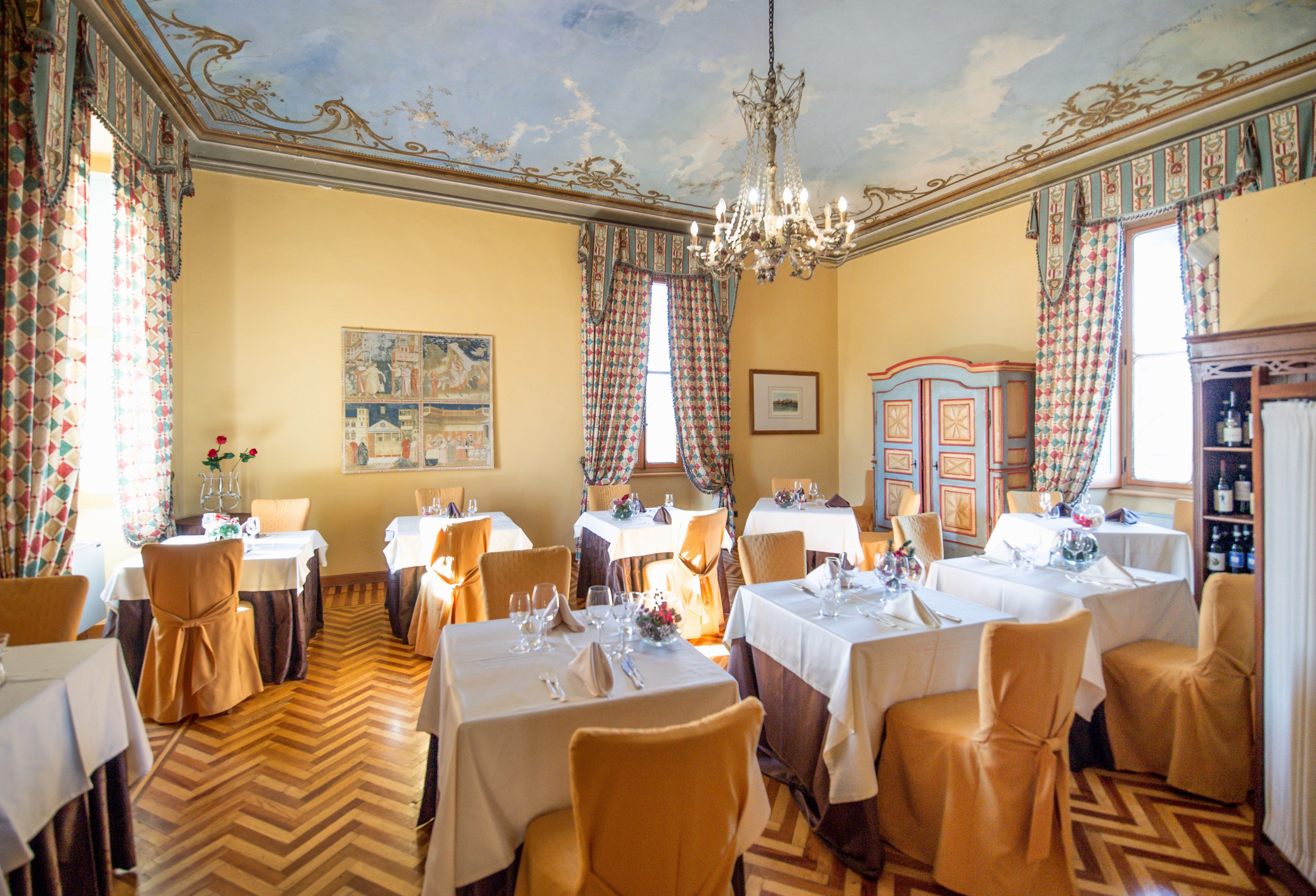 A dining room with multiple tables and chairs, a chandelier, and a patterned ceiling.