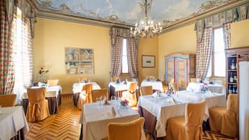 A dining room with multiple tables and chairs, a chandelier, and a patterned ceiling.