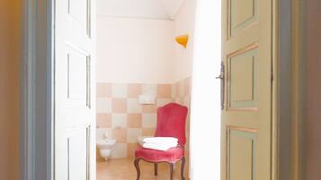 A hallway leading to a bathroom with a red chair, a toilet, and a light fixture.