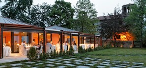 An outdoor dining area with tables and chairs, surrounded by a garden with a stone pathway. - Castello Rosso (Costigliole Saluzzo)