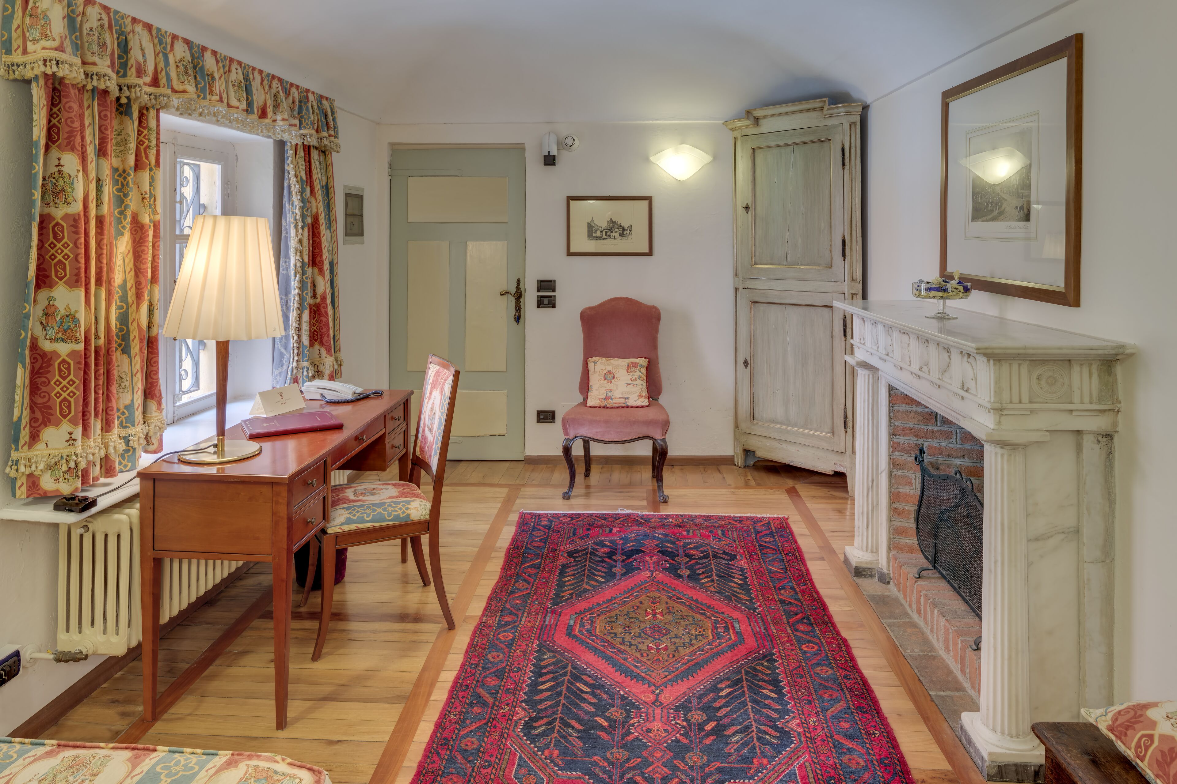 Una habitación tradicional con un escritorio de madera, un sillón rojo, una alfombra estampada y una chimenea.