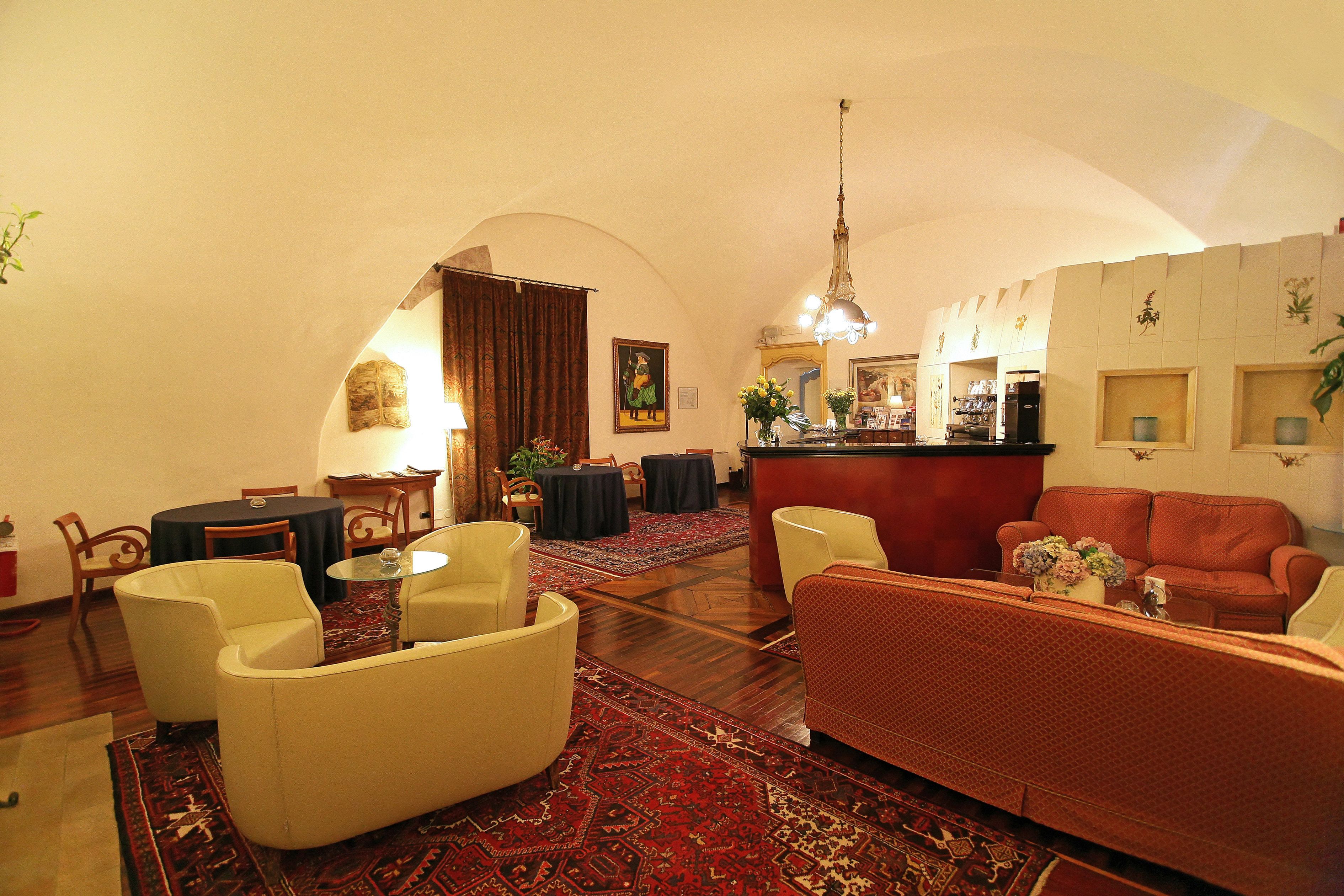 A spacious living area with a red sofa, a yellow armchair, and a beige sofa. There is a dining area with a table and chairs, a bar area with a counter, and a large mirror on the wall.