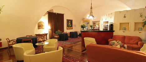 A spacious living area with a red sofa, a yellow armchair, and a beige sofa. There is a dining area with a table and chairs, a bar area with a counter, and a large mirror on the wall.