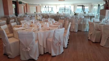 Un salón de banquetes con mesas redondas dispuestas para comer, sillas con fundas blancas y suelo de madera.