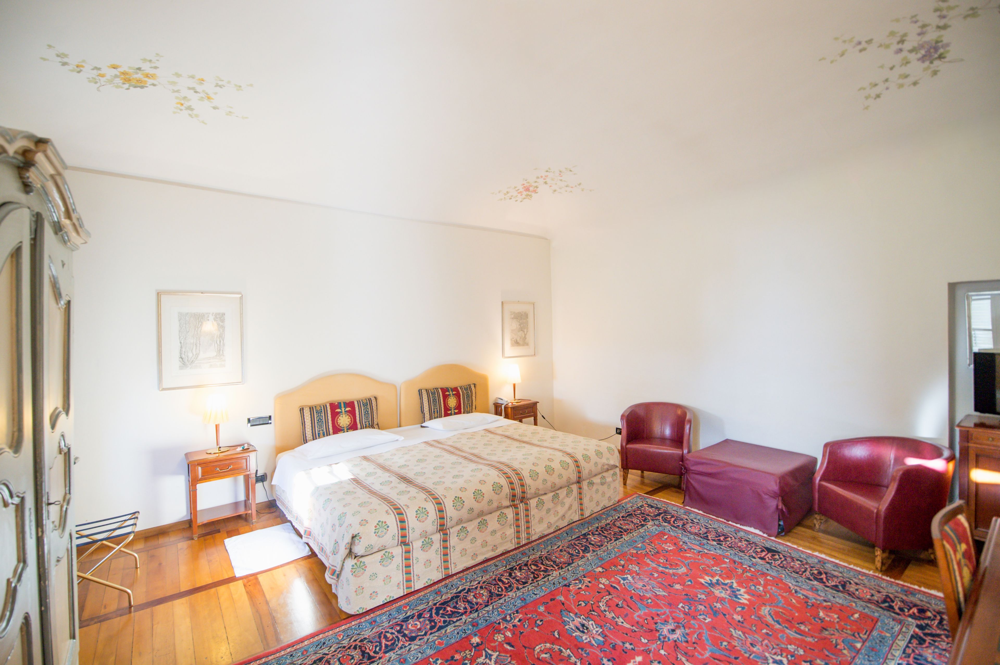 A bedroom with a bed, two nightstands, a red leather chair, a wooden floor, and a patterned rug.