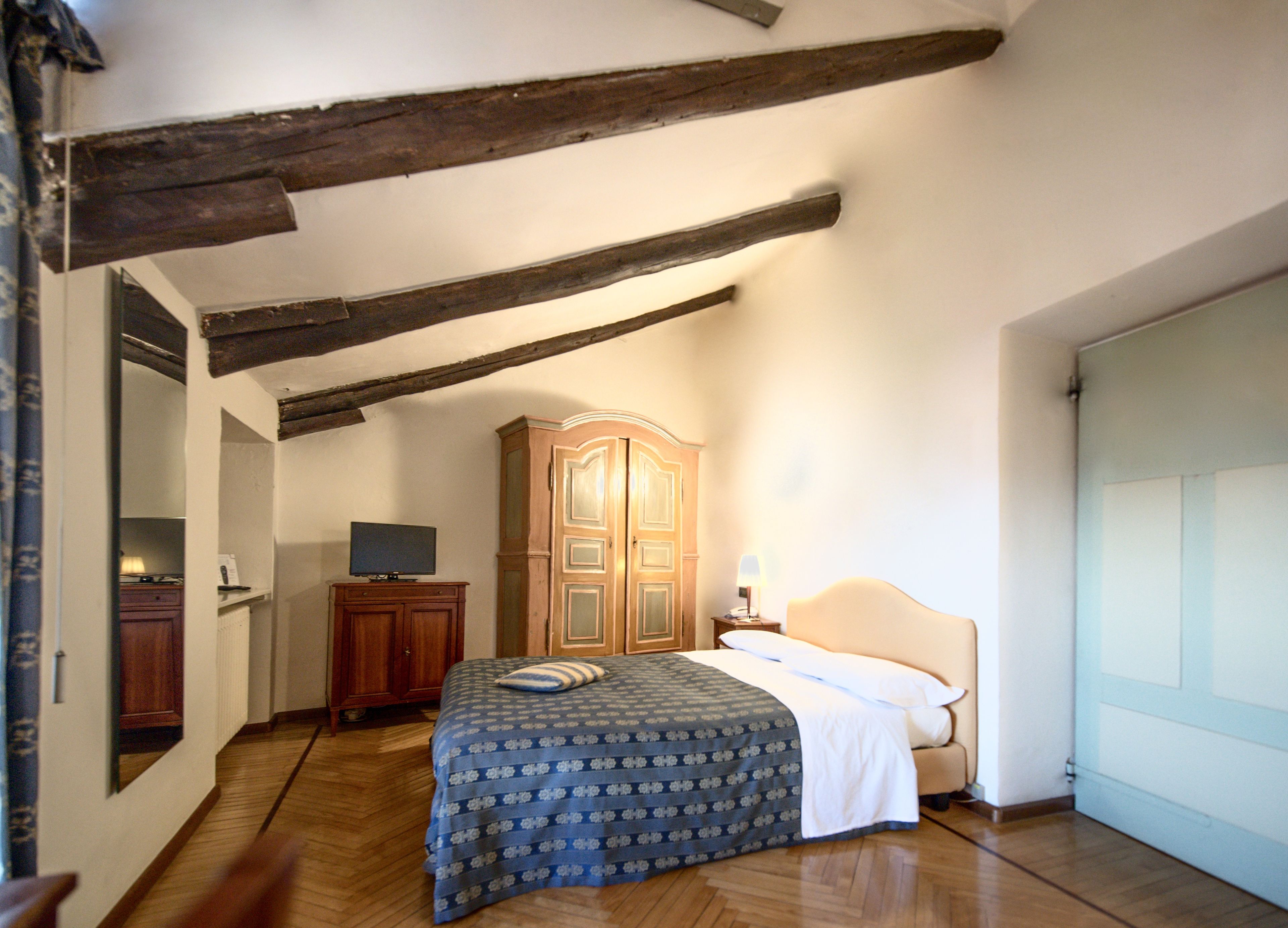 Un dormitorio con cama, armario de madera y televisor sobre un aparador.