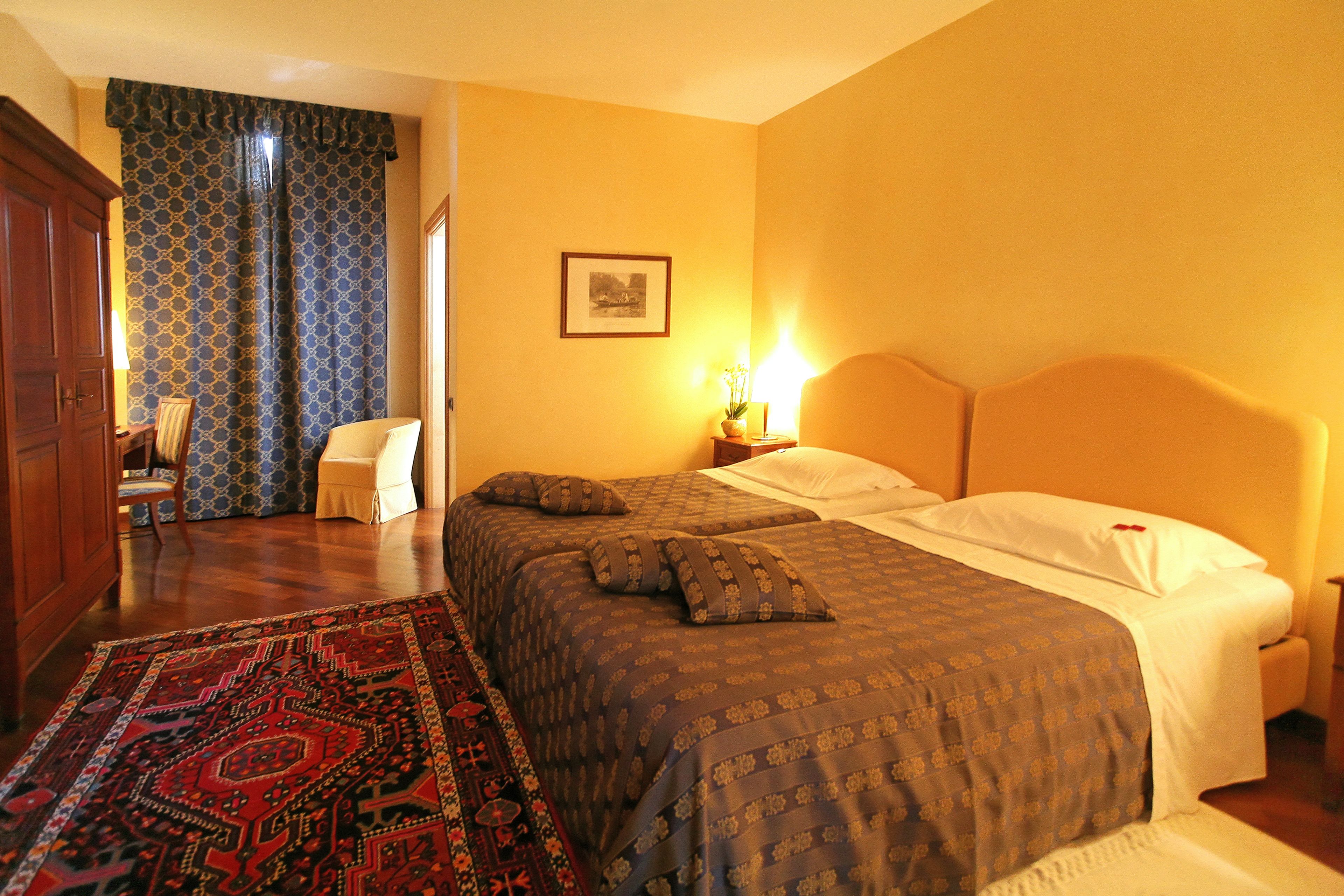 Habitación de hotel con dos camas, un tapete estampado, un armario de madera y un cuadro en la pared.