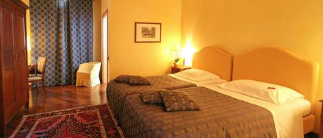 Habitación de hotel con dos camas, un tapete estampado, un armario de madera y un cuadro en la pared.
