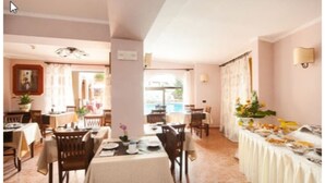 A dining area with tables set for a meal, a buffet line with food, and a view of the outdoors through large windows.