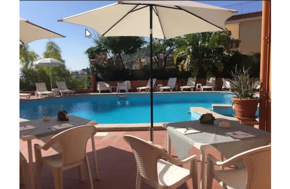 A poolside area with lounge chairs and umbrellas, a dining table, and a view of the pool. - Andromaco Palace Hotel (Taormina)