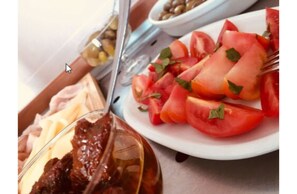 A plate of sliced tomatoes garnished with herbs, a bowl of olives, and a glass of a dark liquid, possibly wine, on a table. - Andromaco Palace Hotel (Taormina)