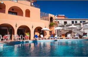 A poolside area with lounge chairs and umbrellas, a clear blue pool, and a building with arched windows and balconies. - Andromaco Palace Hotel (Taormina)