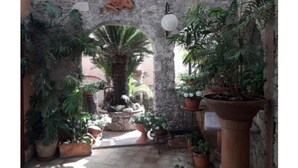 A stone archway with a decorative relief, surrounded by potted plants and a small fountain.