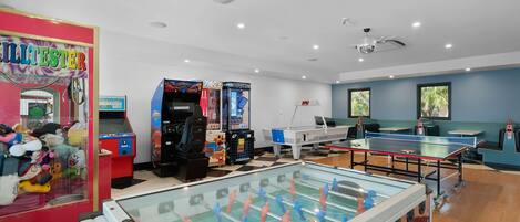 A room with a foosball table, two arcade games, a foosball table, and a red claw machine.