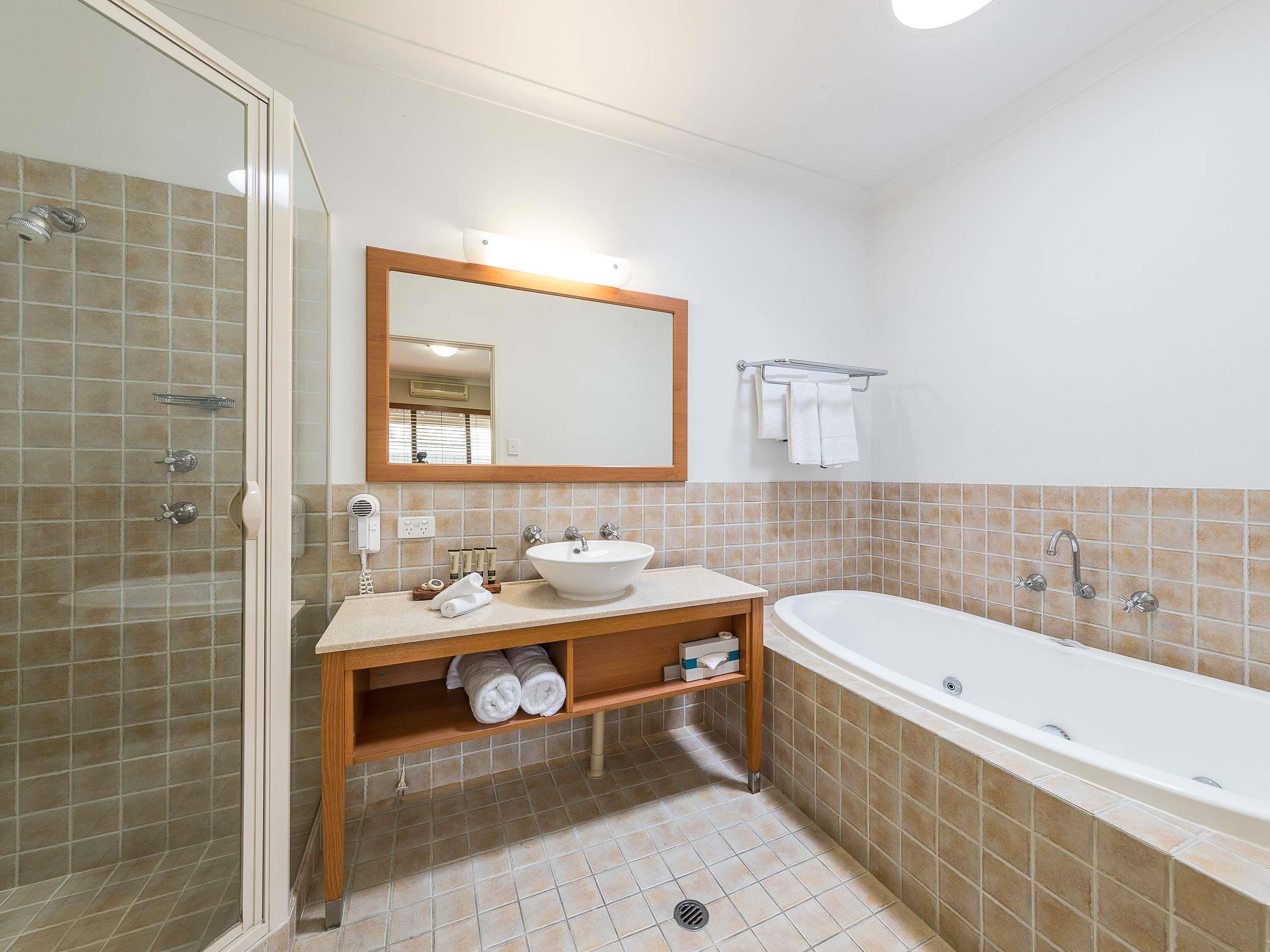 A bathroom with a glass shower enclosure, a sink with a mirror above it, a bathtub, and a towel rack.