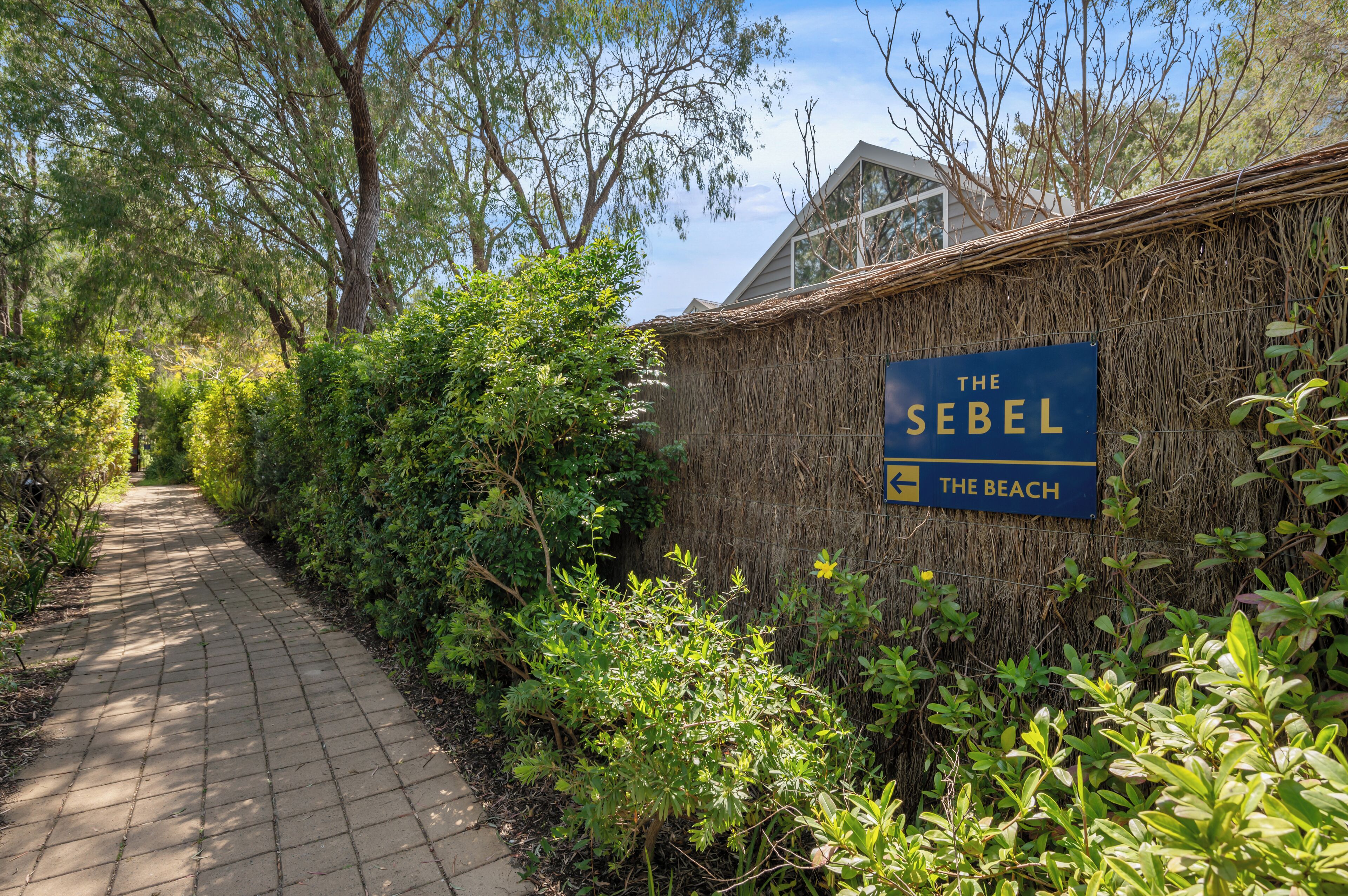 Un chemin menant à un bâtiment sur lequel on peut lire l’inscription : « The Sebel The Beach ».