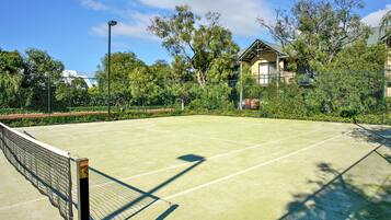Ein Tennisplatz im Freien mit Netz, umgeben von Bäumen und einem Gebäude im Hintergrund.