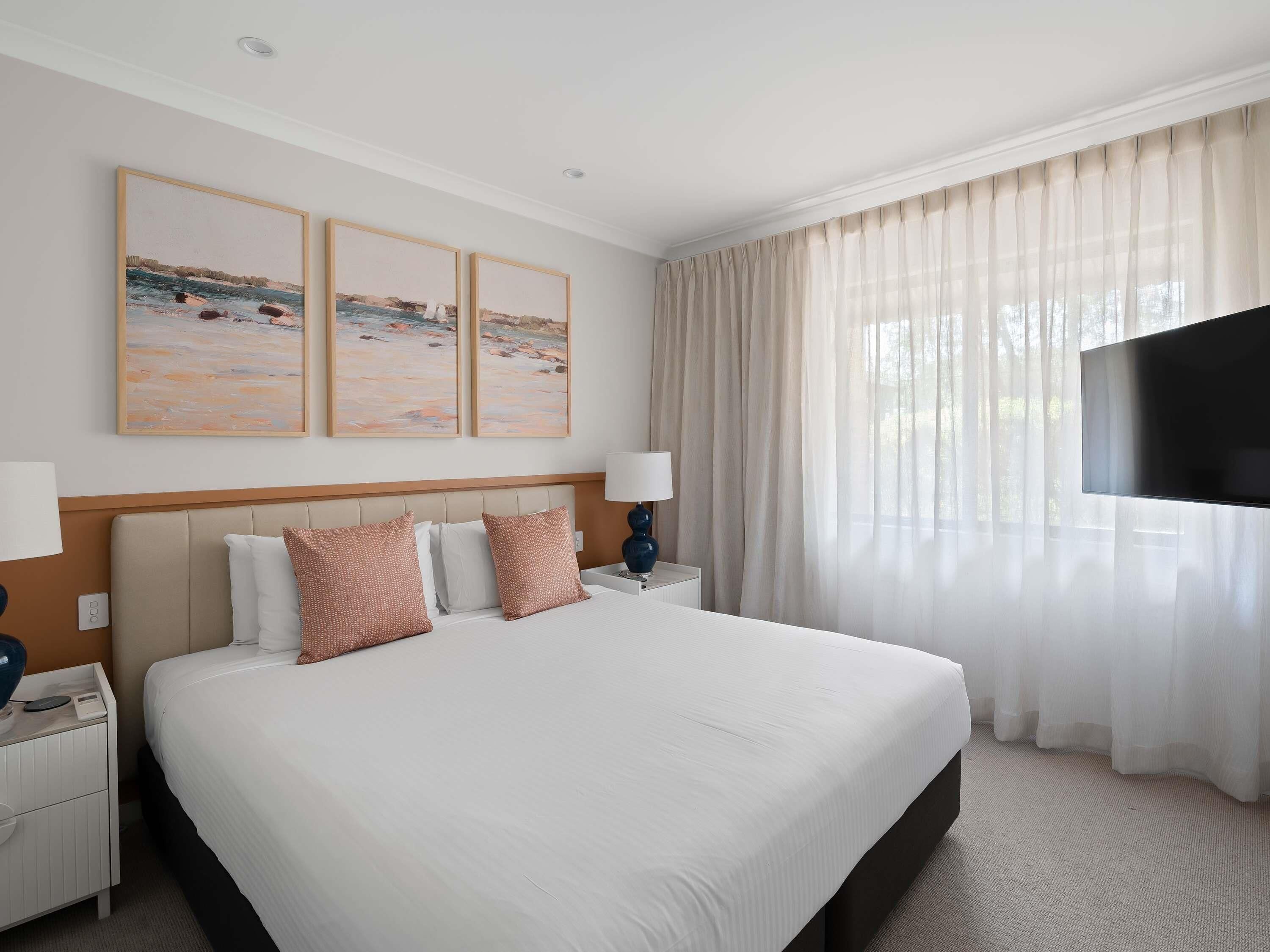 A hotel room with a large bed, two bedside tables, a flat-screen TV, and artwork on the wall.