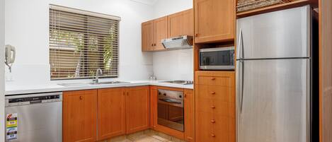 A modern kitchen with wooden cabinets, stainless steel appliances, and a tiled floor.