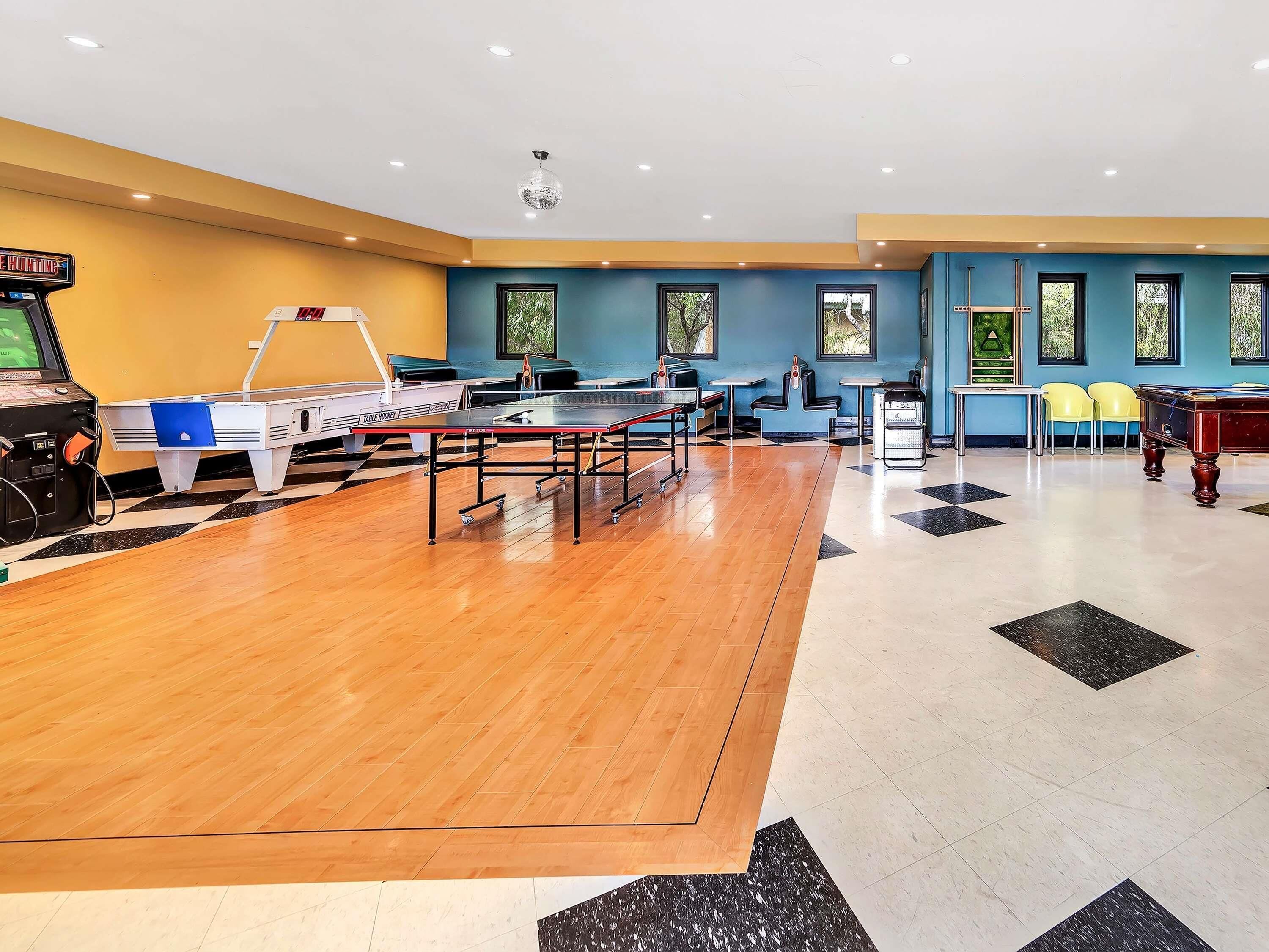 Una sala de billar con varias mesas, una mesa de billar y una mesa de ping pong.
