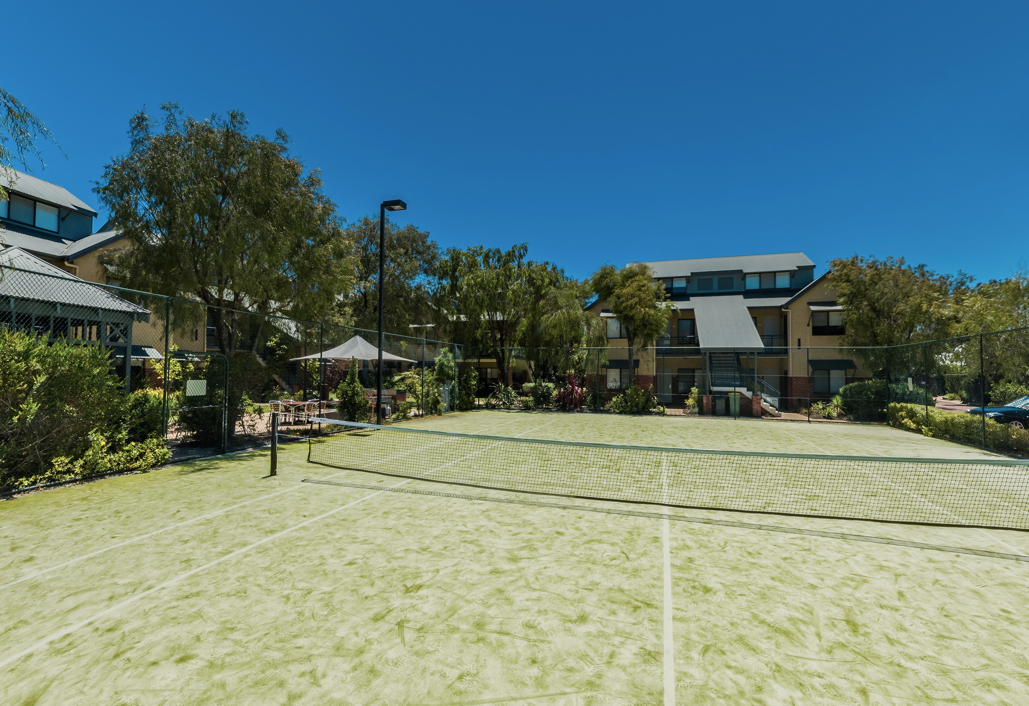 A tennis court with a net, surrounded by trees and buildings.