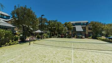 A tennis court with a net, surrounded by trees and buildings.