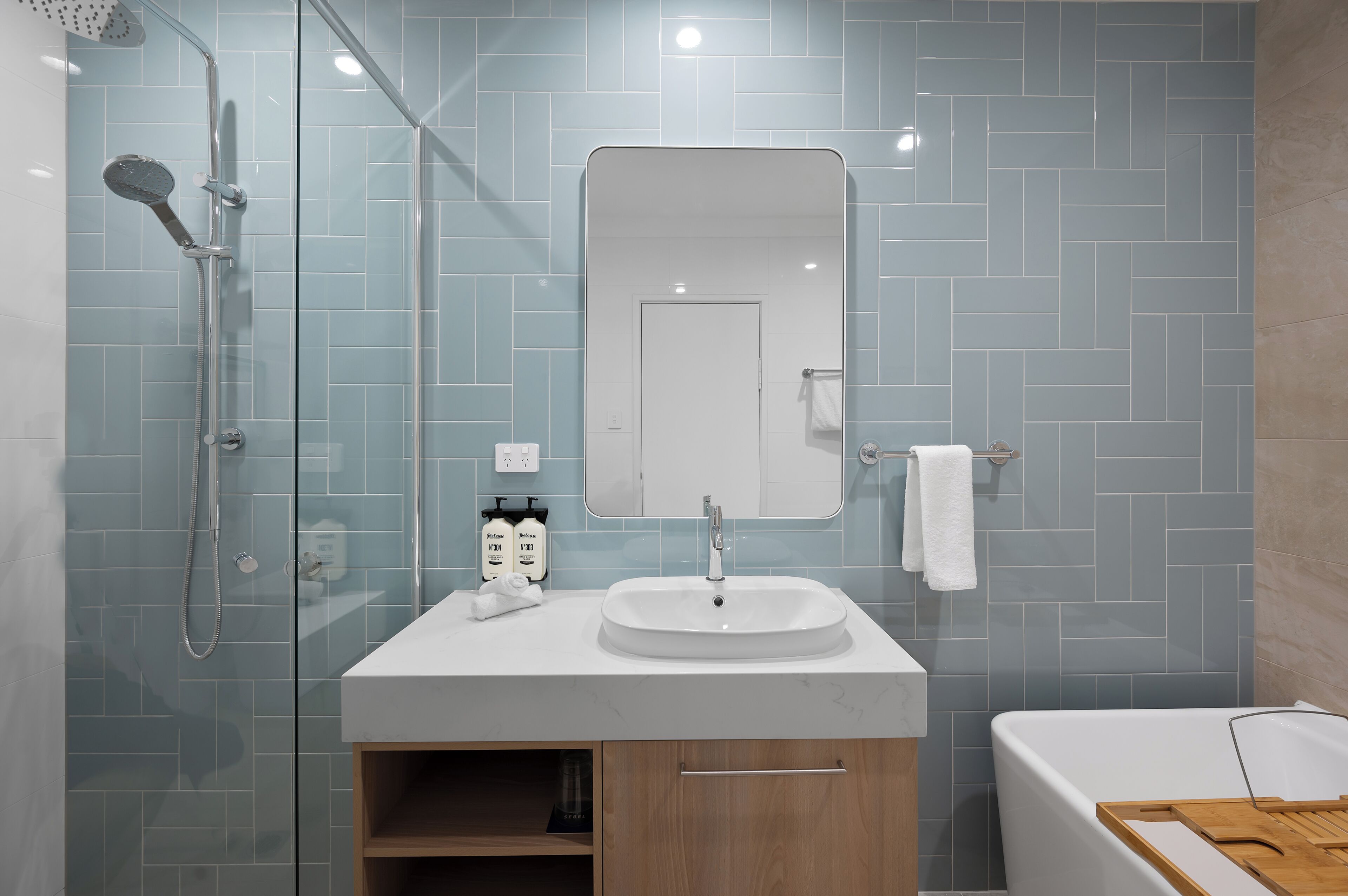 Ein modernes Badezimmer mit einer Glaskabine zur Dusche, einem weißen Waschbecken und einem großen Spiegel.
