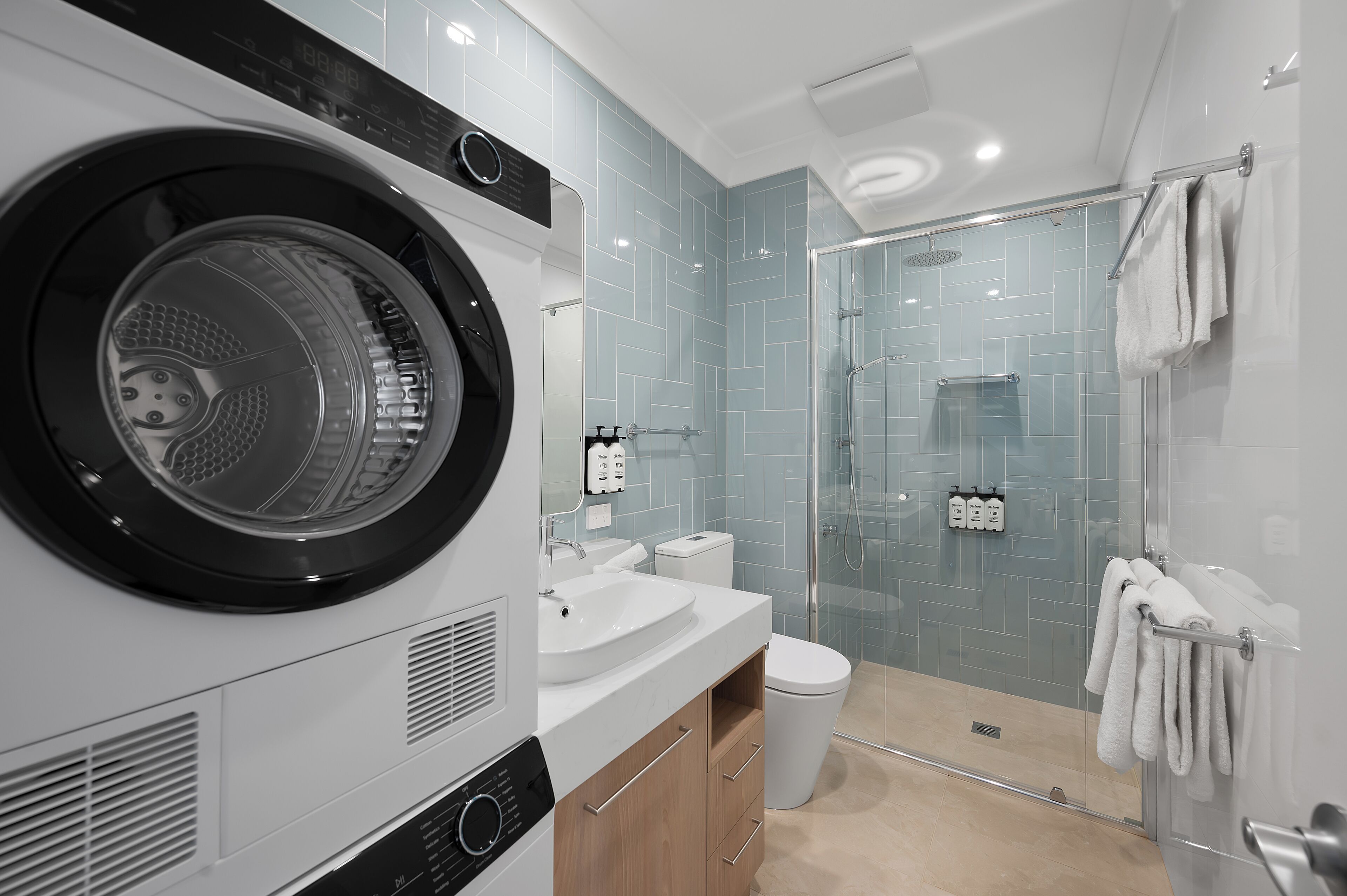 A modern bathroom with a built-in washer and dryer, a glass shower enclosure, and a toilet.