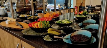 Un bufé con diversos alimentos, entre ellos vegetales en rodajas, encurtidos y recipientes con salsas.