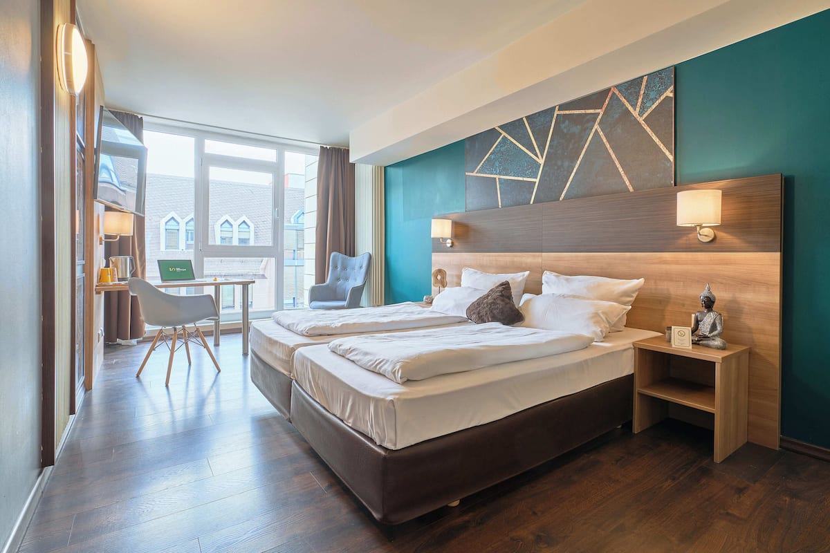 Quarto de hotel com duas camas, uma mesa e uma cadeira.