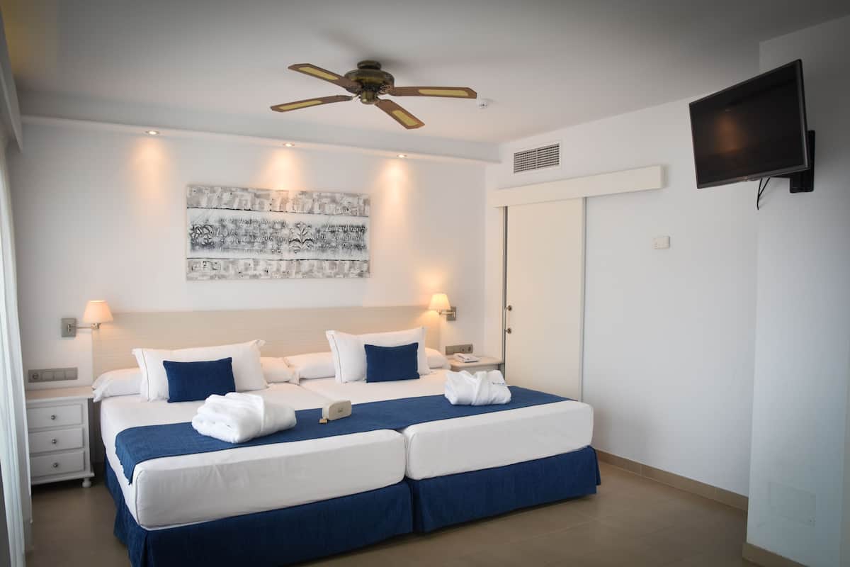 A hotel room with a large bed, a ceiling fan, a flat-screen TV, and a wall-mounted artwork.