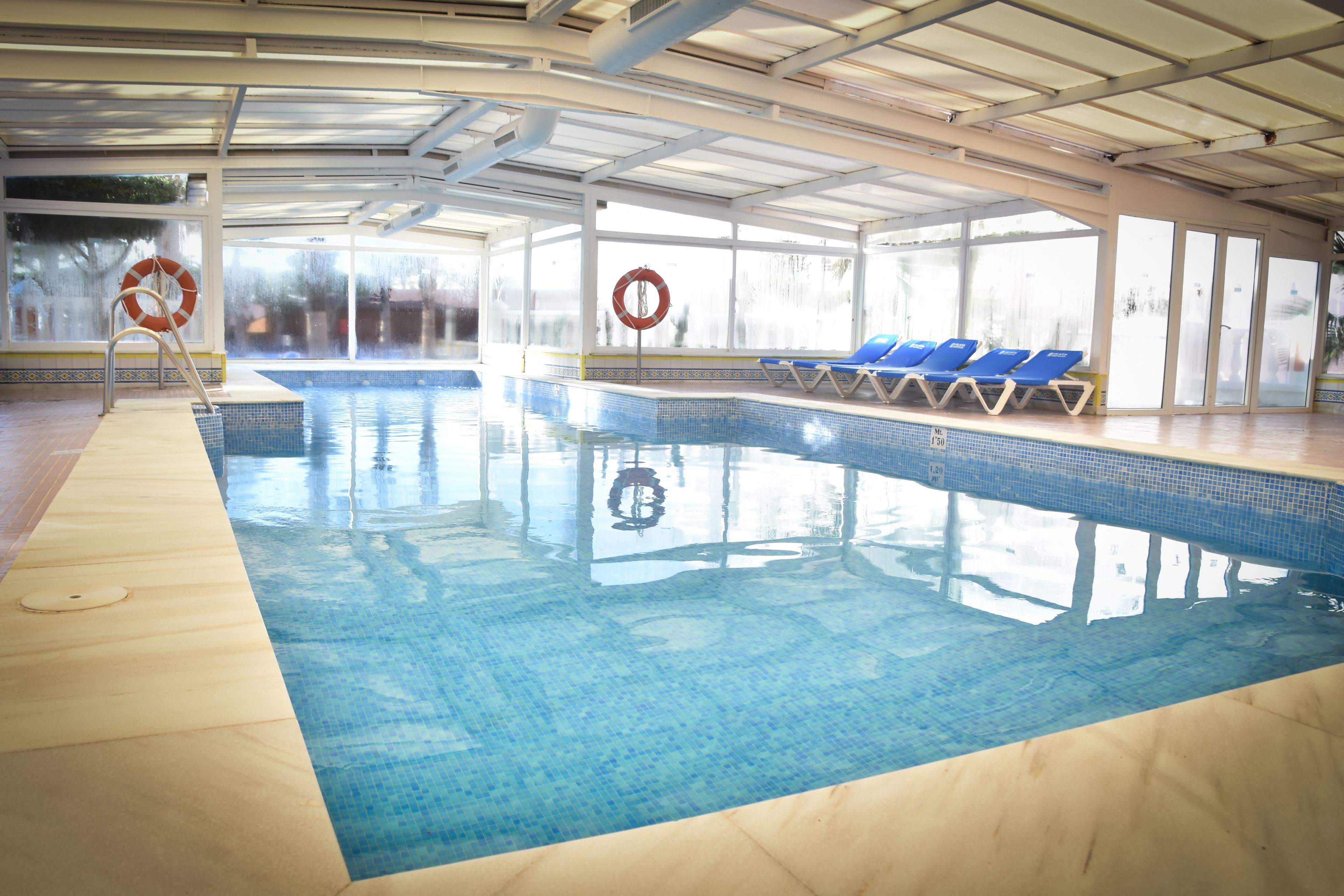 Une piscine intérieure à l’eau claire, avec des chaises longues bleues et des bouées de sauvetage.