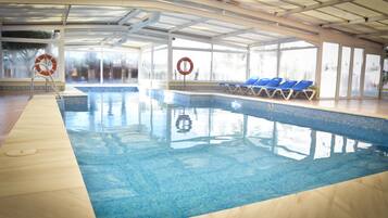 Une piscine intérieure à l’eau claire, avec des chaises longues bleues et des bouées de sauvetage.