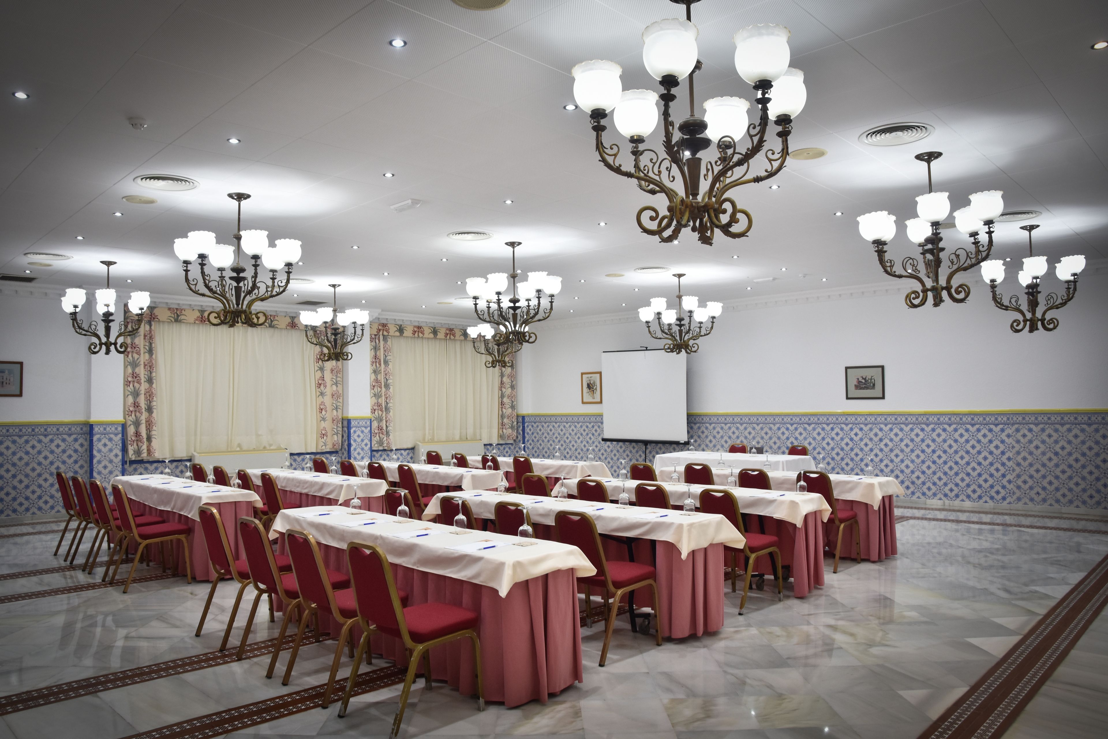 A conference room with multiple tables and chairs, chandeliers, and a whiteboard on the wall.