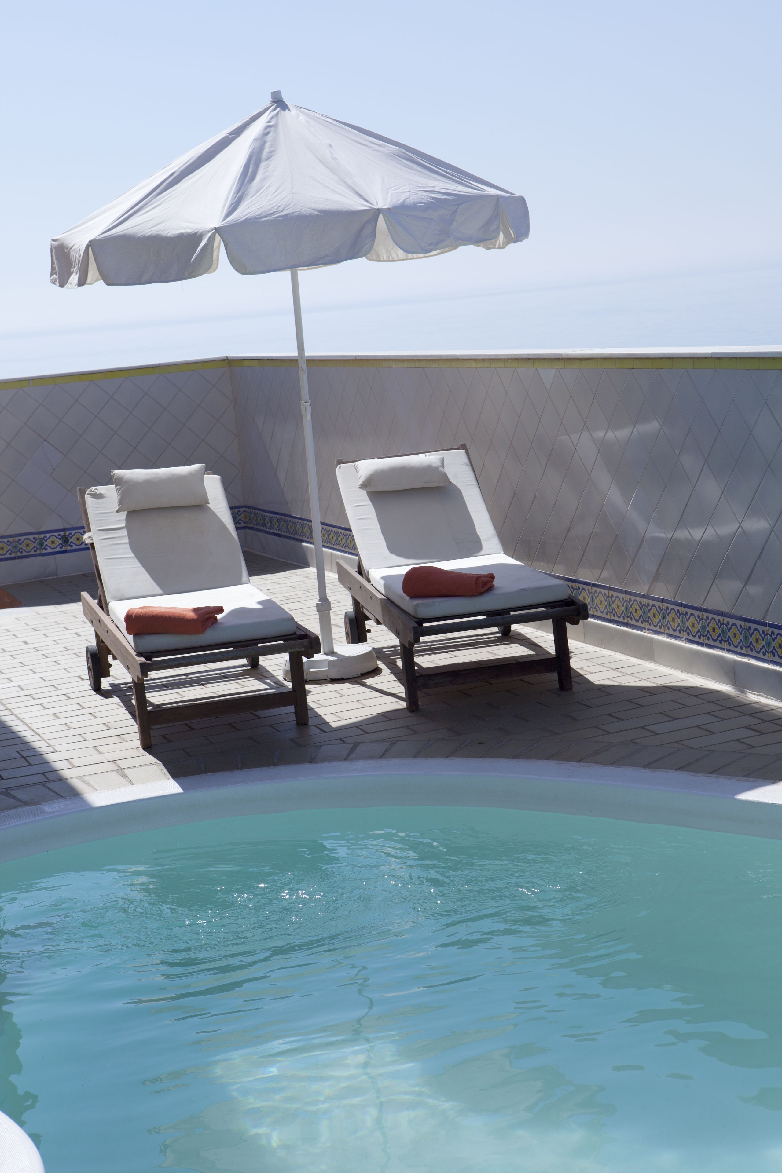 Two sun loungers with towels, a pool, and a tiled wall with a decorative border.