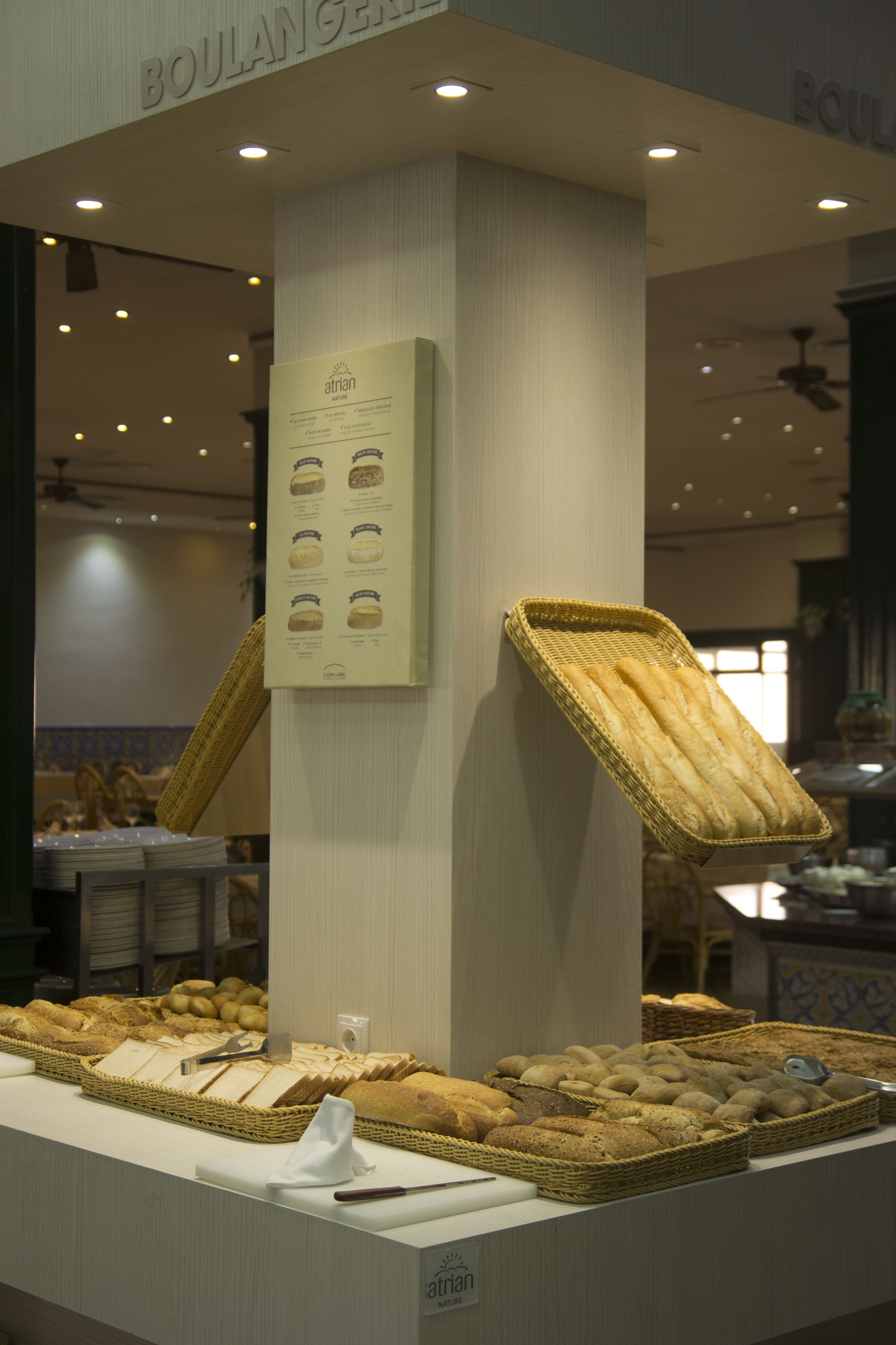 A bakery display with various breads and pastries, a menu board, and a ceiling fan.