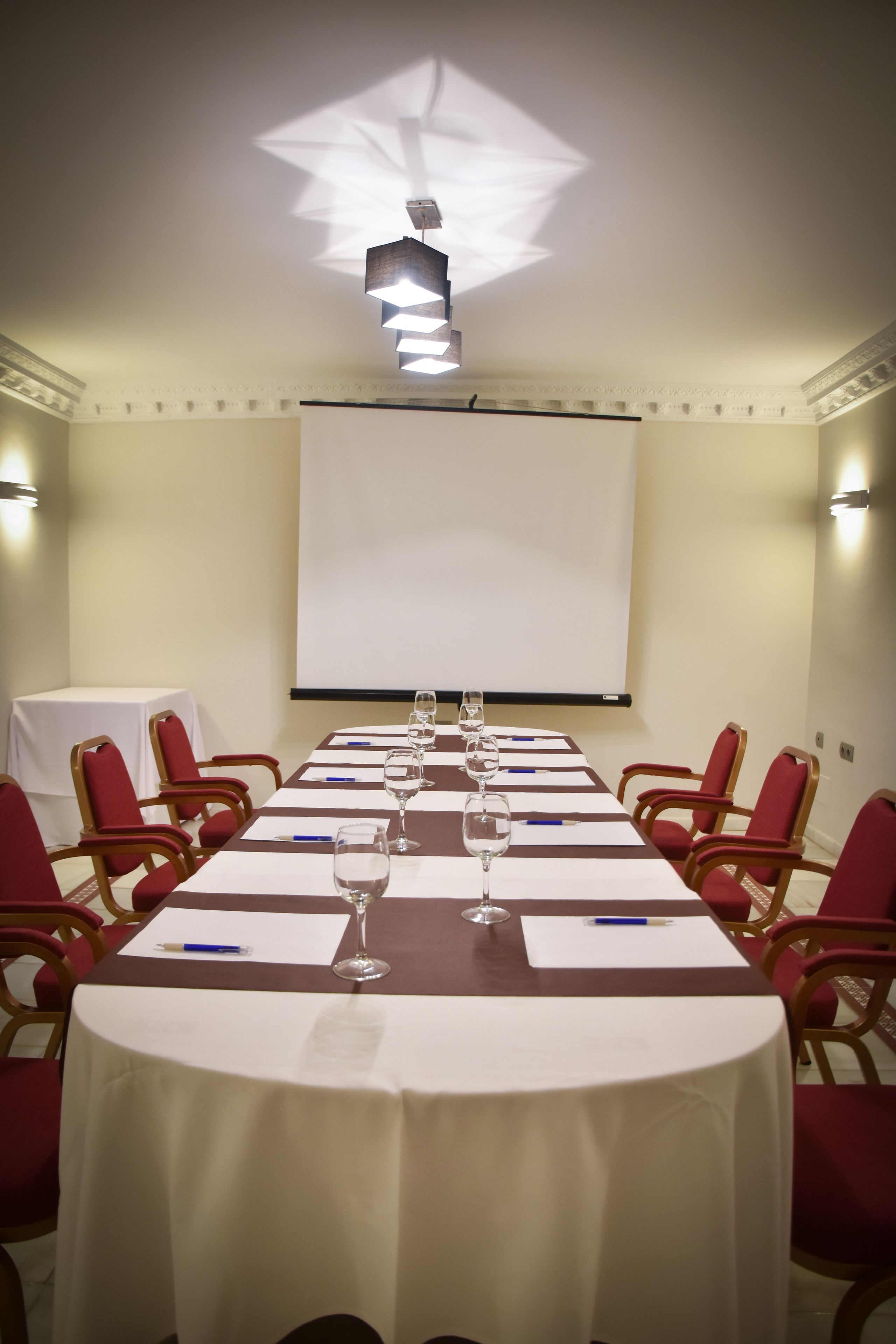 A conference room with a long table, red chairs, and a projector screen.