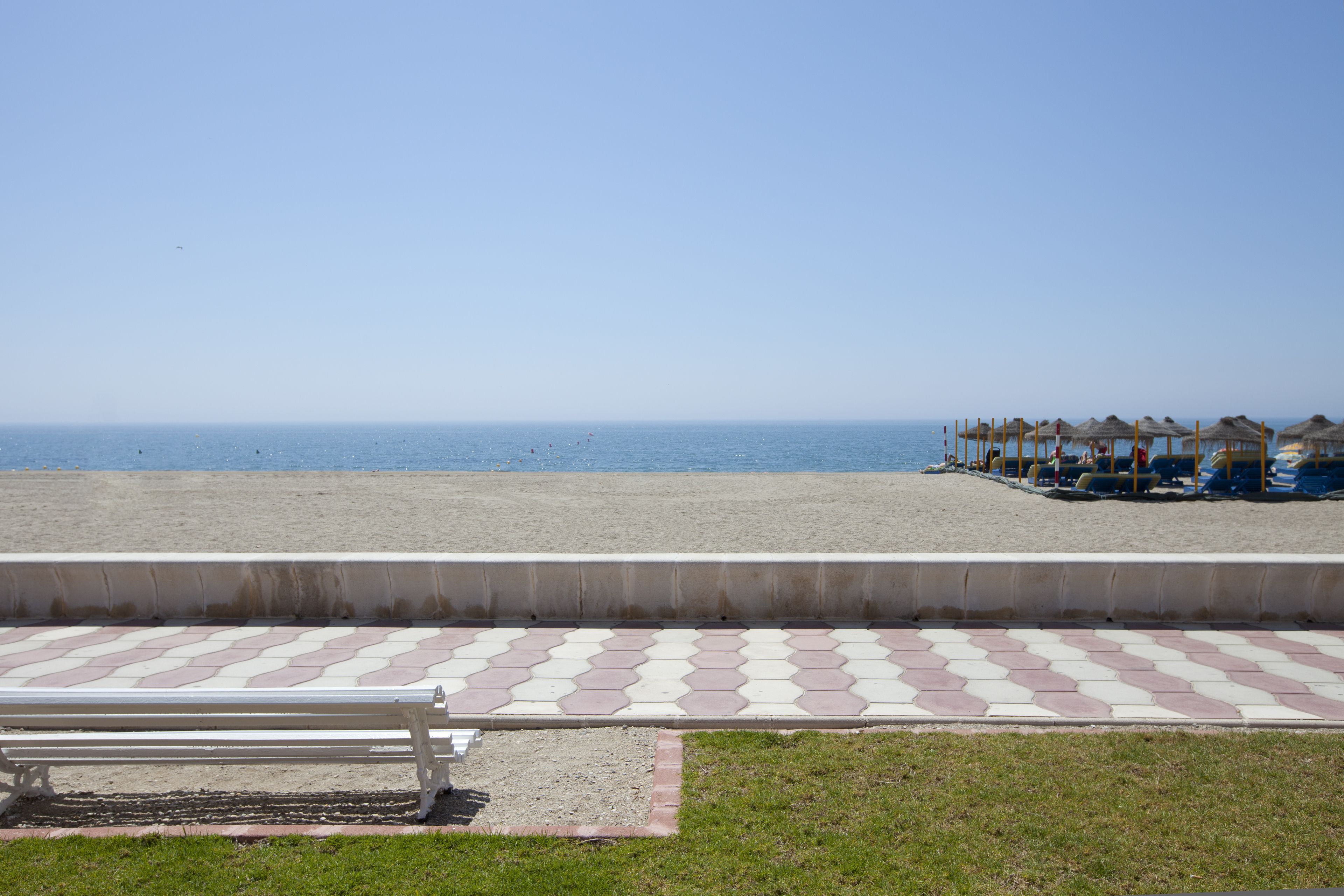 Una playa con un paseo de baldosas, un banco y sombrillas.