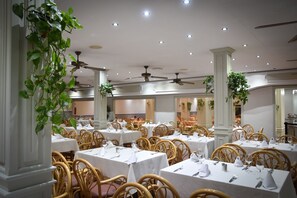 A restaurant with multiple tables and chairs, ceiling fans, and decorative plants. - Playacapricho Hotel (Roquetas de Mar)