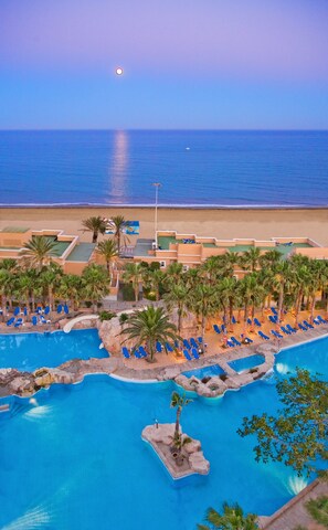 A resort with a pool area, palm trees, and a view of the ocean. - Playacapricho Hotel (Roquetas de Mar)