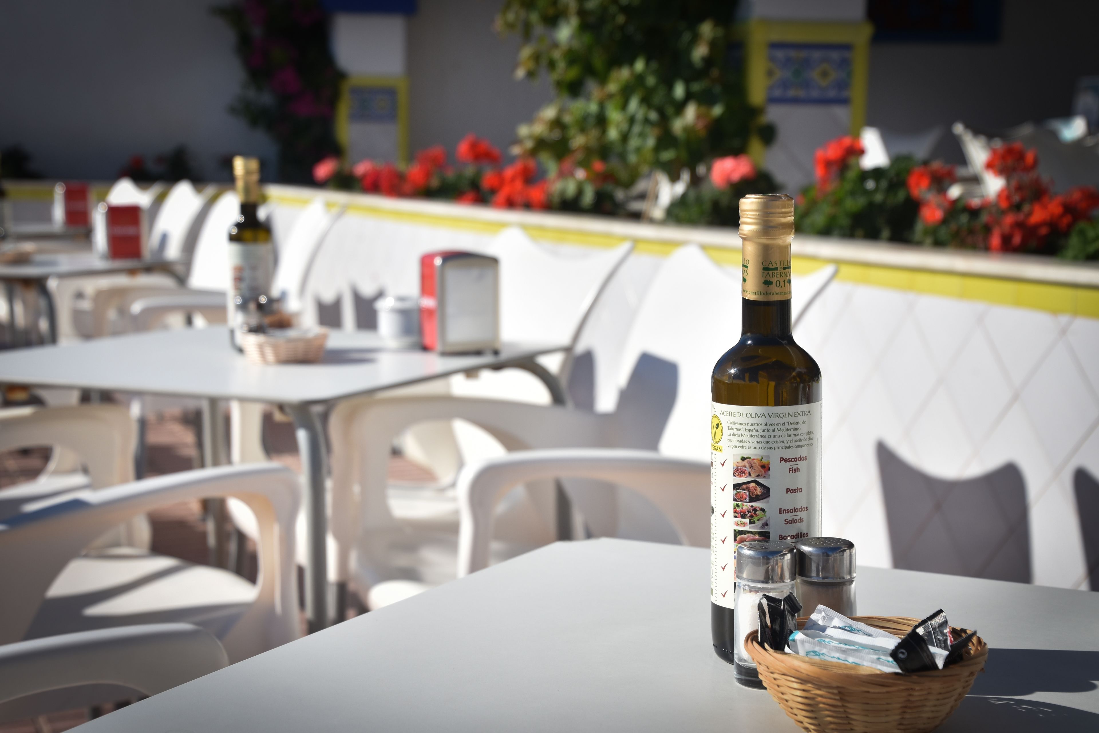 Une table avec une bouteille d’huile d’olive, des salières et des poivrières, et un panier de collations, le tout dans un décor de restaurant.