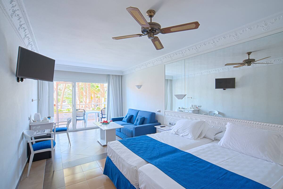 A hotel room with a bed, a desk, a chair, a TV, and a ceiling fan.