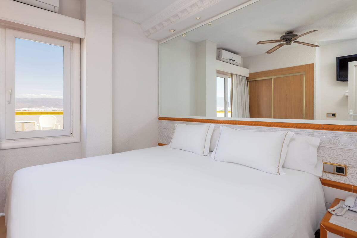 A hotel room with a large bed, a ceiling fan, a mounted TV, and a window with a view.