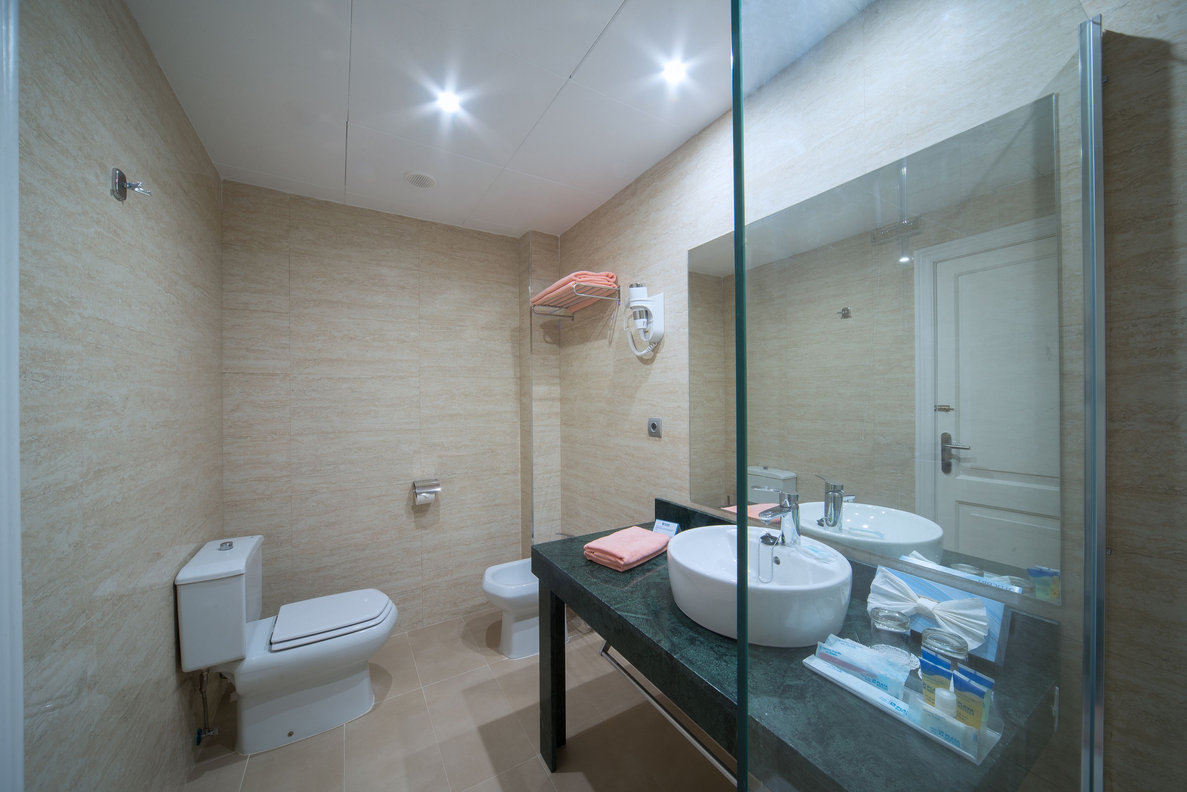 Un baño moderno con inodoro, bidé y tocador con lavamanos y espejo.