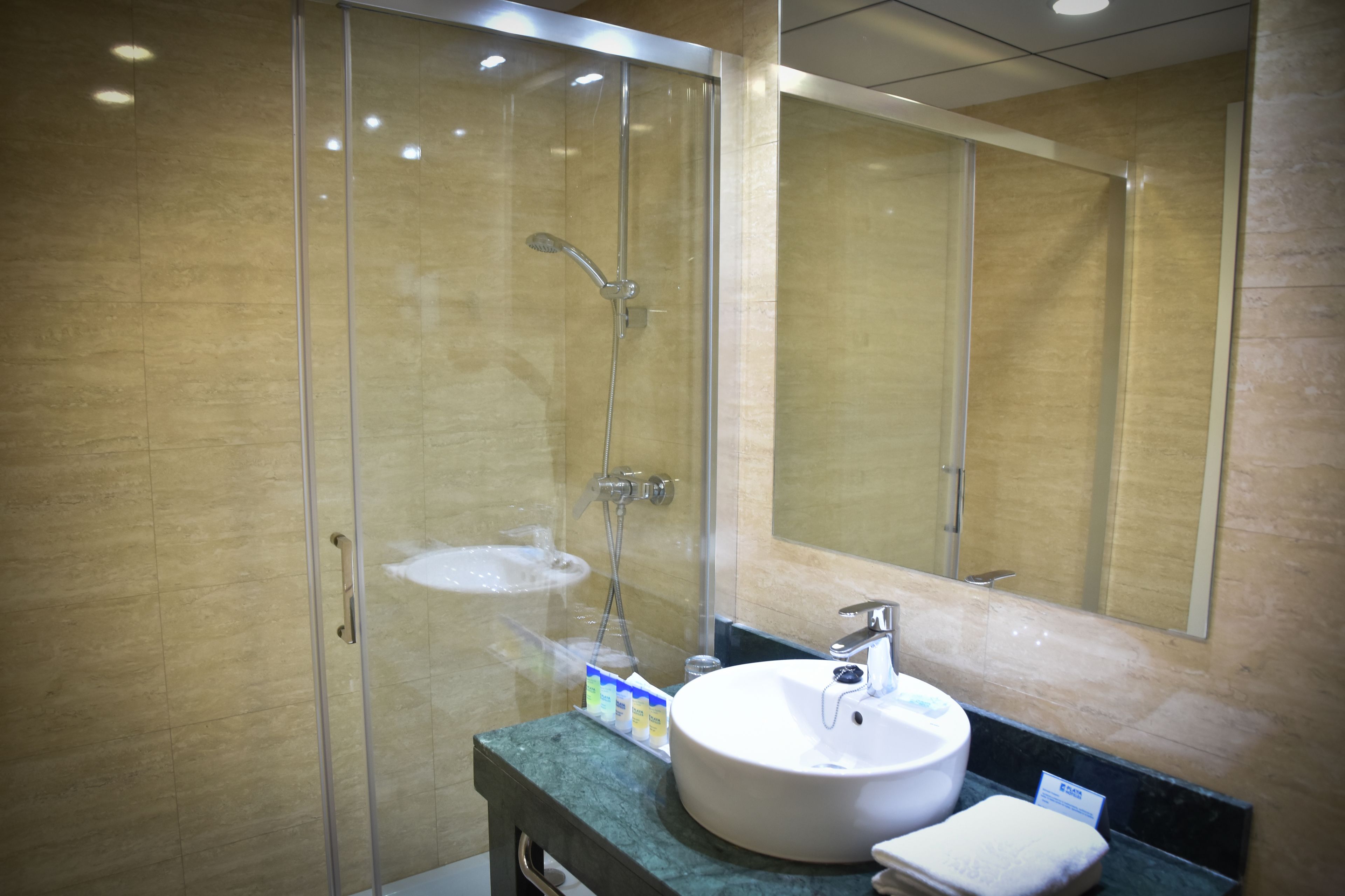 Un baño moderno con ducha de vidrio, lavamanos redondo y un espejo grande.